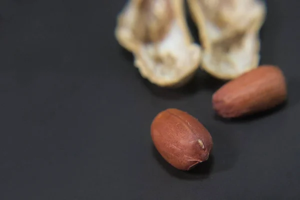 Cracked Shelled peanut with two nuts inside on a black surface