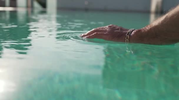 Un homme avec un bracelet au poignet plonge sa main dans la piscine — Video
