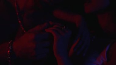 Çift birbirini okşuyor. Elleri neon ışıkta.