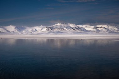 ARKTİK NORASINDA SVALBARD NORASI 'nın yanında küçük bir buzul kanalı ve okyanusta bir kayalık ile kaplı kar örtülü bir dağ.