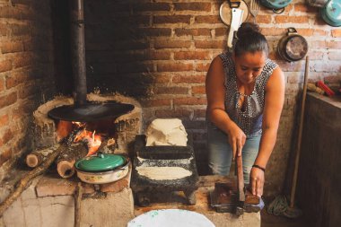 Meksika 'lı bir kadın tortilla yapmak için bir metastaz ve odun sobasında mısırlı sprey hazırlıyor.