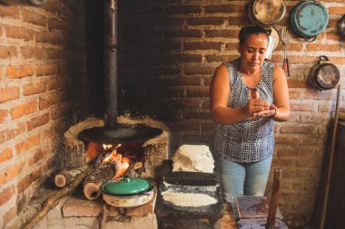 Meksika 'lı bir kadın tortilla yapmak için bir metastaz ve odun sobasında mısırlı sprey hazırlıyor.