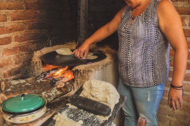 Meksika 'lı bir kadın tortilla yapmak için bir metastaz ve odun sobasında mısırlı sprey hazırlıyor.