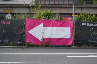 Üzerinde pembe bir poster ve solu gösteren beyaz bir ok olan bir ilan panosu.