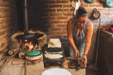 Meksika 'lı bir kadın tortilla yapmak için bir metastaz ve odun sobasında mısırlı sprey hazırlıyor.