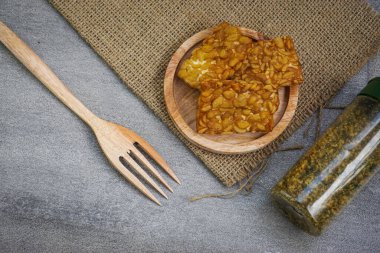 Ahşap çatal ve biber tozu şişesinin yanında, mutfaktaki ahşap tabakta kızartılmış tempeh yakın çekim.