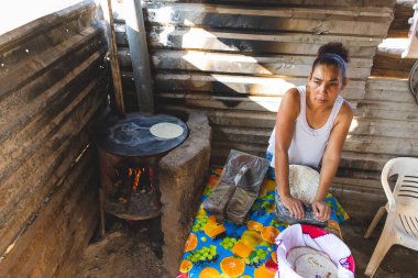 Mexican woman torturing corn mace on a metate and wood stove to make homemade tortillas in cuautla, jalisco, mex clipart