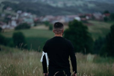 Kolunun üst kısmına beyaz bir bez parçası bağlanmış siyah uzun kollu bir adamın arka görüntüsü.