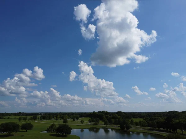 湖と公園の上にふわふわの雲と青い空の低角度ショット — ストック写真
