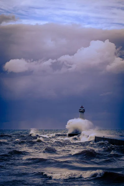 A vertical shot of waves crashing against a lighthouse on a pier on Sodus Bay, New York