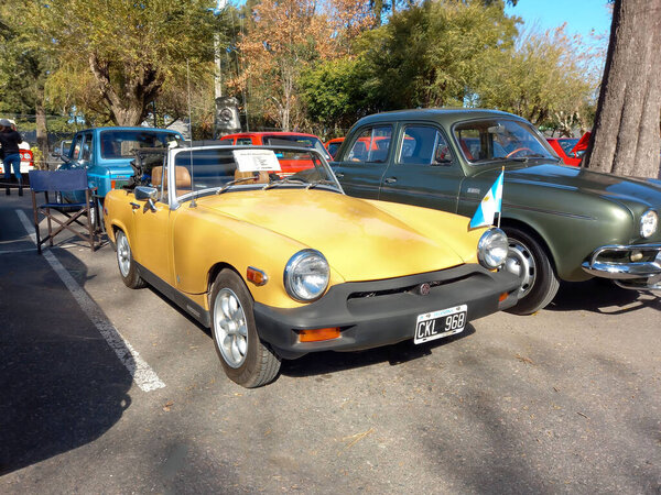 Quilmes, Argentina - May 29, 2022: Old yellow sport MG Midget 1500 1976 two door convertible in a park. Nature, trees. Classic car show. Copyspace