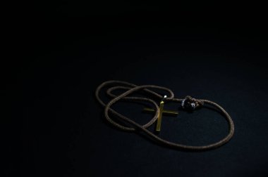 Altın renkli Hıristiyan haçı ve siyah arka planda iple gerilmiş kolye.