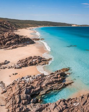 Dikey kayalıkları olan kumlu bir sahil manzarası.