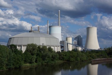 Almanya 'nın Hanau kenti yakınlarındaki Main nehrindeki Staudinger kömür yakıtlı elektrik santrali akşam vakti çalkantılı bir gökyüzüne karşı. Kömür deposu ön planda.