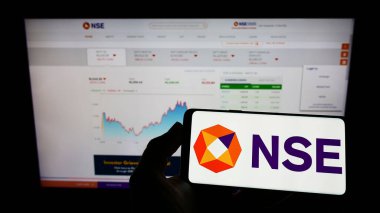 Hindistan Ulusal Borsası (NSE) logosu web sayfasının önünde ekranda olan cep telefonu sahibi. Telefon ekranına odaklan.
