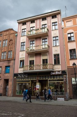 Polonya 'nın Torun kentindeki geleneksel binaların altında dükkanların önünde yürüyen insanların dikey görüntüsü