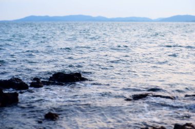 Güneşli bir günde kumsalda kayaları yıkayan mavi deniz dalgalarının manzarası.