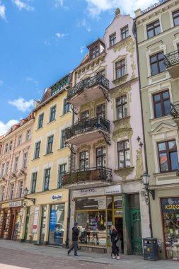 Polonya 'nın Torun kentindeki geleneksel binaların altında dükkanların önünde yürüyen insanların dikey görüntüsü