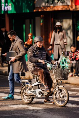 Şangay, Çin sokaklarında kask takmış bisiklet süren yaşlı bir adamın dikey görüntüsü.