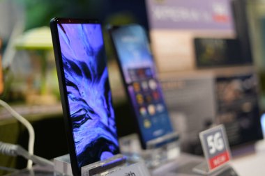 Bulanık bir arka planda bir mağazada sergilenen yeni bir modern akıllı telefonun yakın plan görüntüsü.