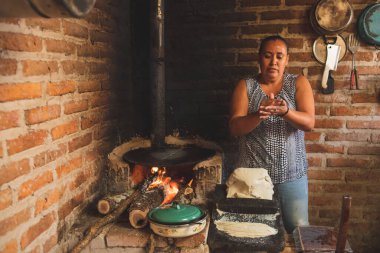 Meksika 'lı bir kadın tortilla yapmak için bir metastaz ve odun sobasında mısırlı sprey hazırlıyor.