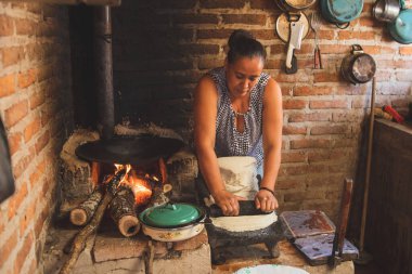 Meksika 'lı bir kadın tortilla yapmak için bir metastaz ve odun sobasında mısırlı sprey hazırlıyor.