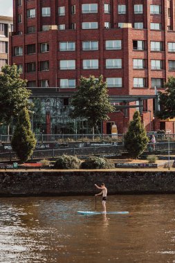 Genç bir adam, şehir binalarının arka planına karşı nehirde bir kano sürüyor.