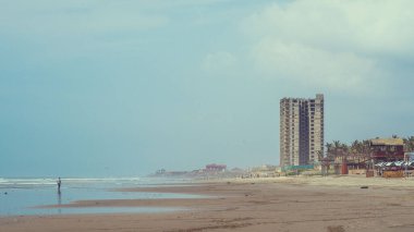 Sahilde tek başına, deniz kenarında, diğer tarafında yüksek binalar olan bir adamın güzel bir fotoğrafı.