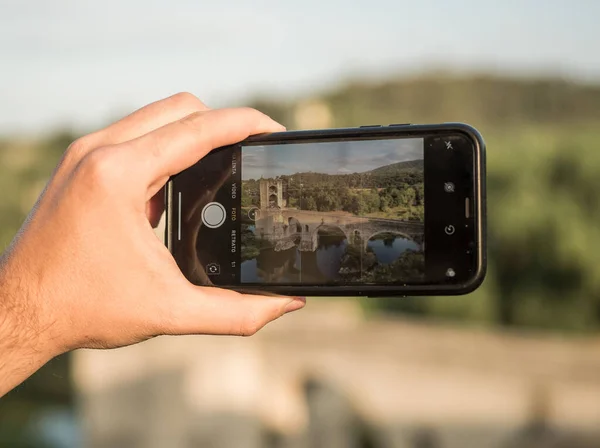 携帯電話を持っている手とベスバルの古代の橋をキャプチャ カタルーニャ州 — ストック写真