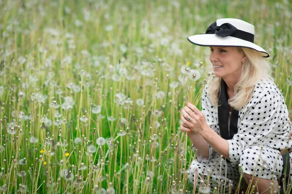 タンポポの畑で帽子をかぶっている美しいブロンドの女性 — ストック写真