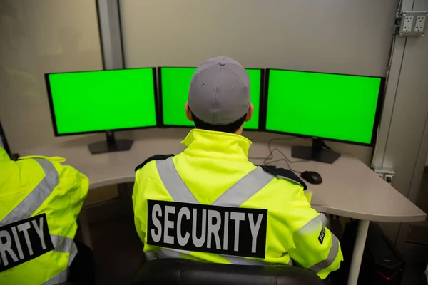 A security team watching over CCTV surveillance monitors with green screen.