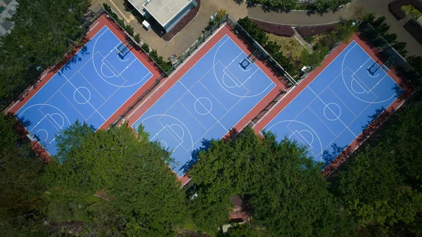 An aerial shot of three empty basketball courts next to each other surrounded with trees