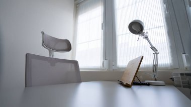 Masasında ışık, tablet standı ve arka planında beyaz sandalye olan modern bir ofis odası.