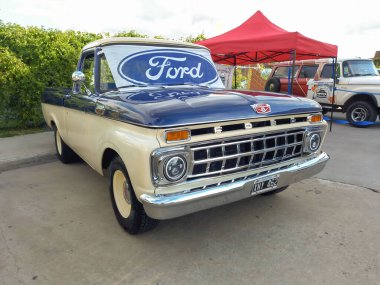 1963 model eski bir F100 kamyonetin ön camında Ford mavi oval logosu ve marka bayrağı vardı. Ön Manzara. Fierros Fuarı 2022 Klasik araba fuarı