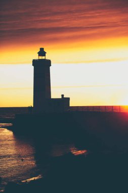 Bulutlu bir günbatımına karşı bir deniz fenerinin siluetinin dikey çekimi
