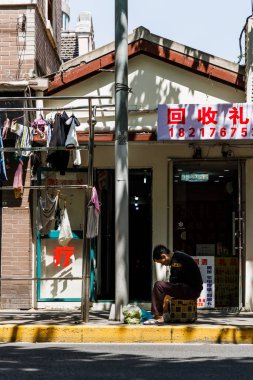 Küçük bir dükkanın önünde oturan bir adamın dikey görüntüsü.