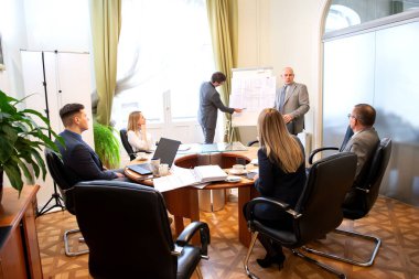 Modern ofisteki iş arkadaşlarıyla birlikte çalışırken yeni proje sunan başarılı iş adamları