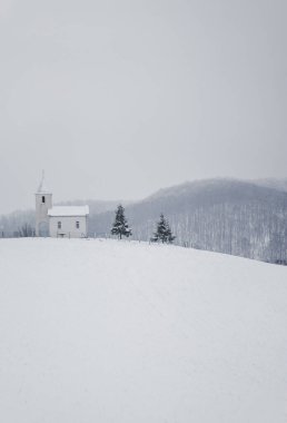 A vertical shot of a small white church on top of a snowy hill in Northern Bosnia and Herzegovina. clipart