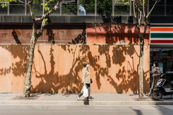 Kobieta Masce Medycznej Chodząca Ulicy Pod Pomarańczową Ścianą Cieniami Drzew — Zdjęcie stockowe