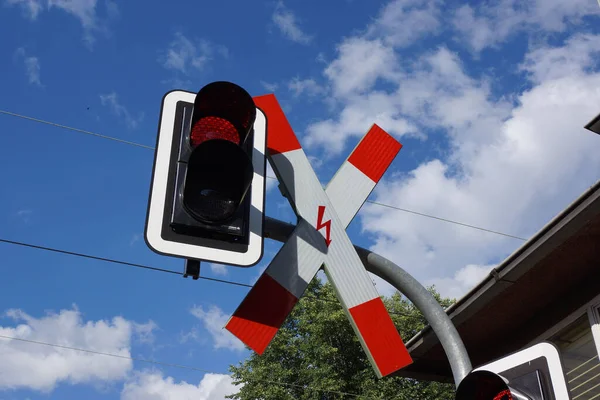 Railway crossing sign and red traffic light over a level crossing against a blue sunny sky. Nice colourful contrast. German traffic sign no. 201-51.