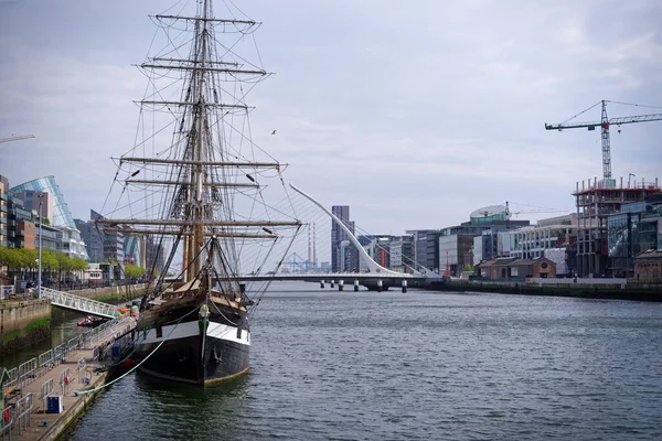 Dublin 'deki Liffey Nehri. Ünlü uzun gemi Jeanie Johnston solda demirlemiş. Arka plandaki Samuel Beckett köprüsü ve ofis binaları.