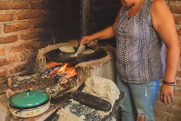 Meksika 'lı bir kadın tortilla yapmak için bir metastaz ve odun sobasında mısırlı sprey hazırlıyor.