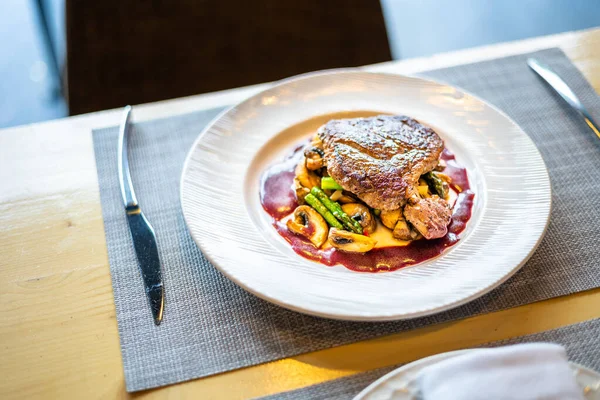 Beyaz bir tabakta ızgara sebzeler üzerinde bir bifteğin yüksek açılı görüntüsü.