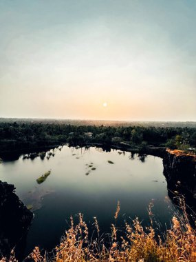 Gün batımında yemyeşil ağaçlarla çevrili küçük bir göl manzarası.