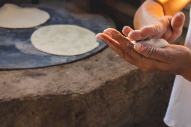 Meksikalı bir kadın, cuautla, jalisco, mex 'te ev yapımı tortilla yapmak için soba ve odun sobasında mısırlara işkence ediyor.