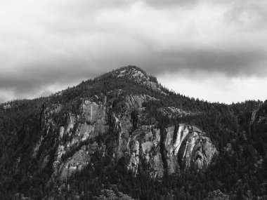 Bulutlu bir gökyüzünün altındaki kayalıkların gri tonlu görüntüsü..