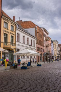 Polonya 'nın Torun kentindeki geleneksel binaların altında dükkanların önünde yürüyen insanların dikey görüntüsü
