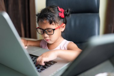 Evdeki oturma odasında dizüstü bilgisayarda yazan Güneydoğu Asyalı sevimli küçük bir kız.