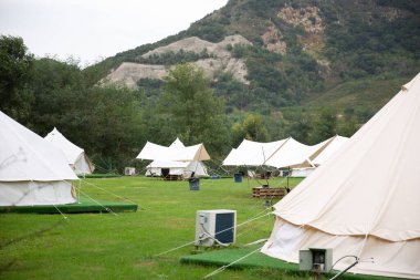 Kamp için beyaz çadırları ve arka planda yeşilliklerle kaplı dağları olan yeşil bir tarla.