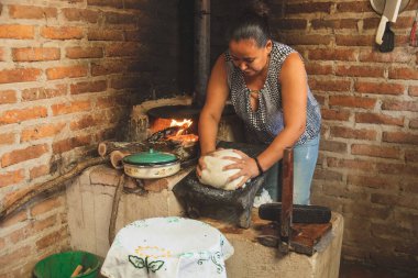 Meksika 'lı bir kadın tortilla yapmak için bir metastaz ve odun sobasında mısırlı sprey hazırlıyor.